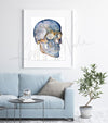 Framed watercolor painting of a skull from a three quarter view. The painting is hanging over a blue couch.